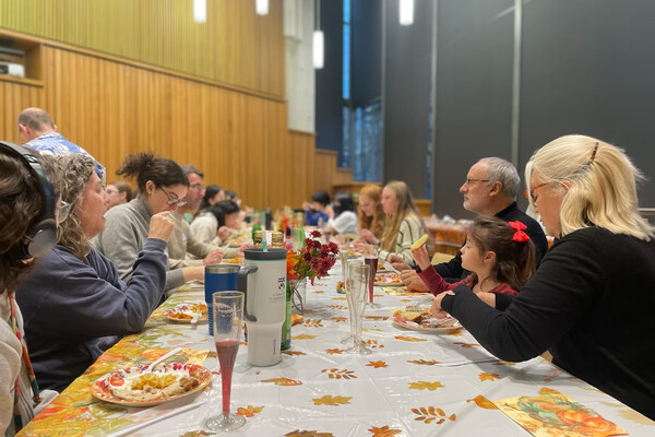 A group of people sit together at a long table with plates of food and Thanksgiving decor