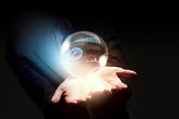 A hand holding a crystal ball with finance charts and graphs inside.