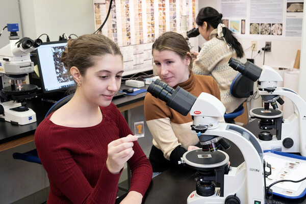 Two students looking at slides under a microscope in a lab.