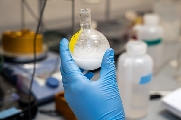 A gloved hand holding a beaker of lipids in a lab.