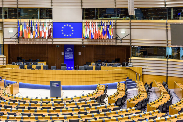 A room full of desks is where the European Parliament meets in Brussels. The flags of the member countries and the European Union are at center.