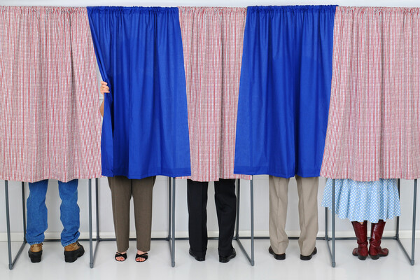 five people standing behind curtains at a polling place.