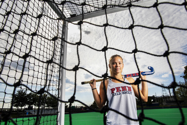 Schneck holding a field hockey stick posing on the field hockey field