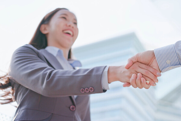 closeup of a young woman in a suit shaking hands with another person off-camera