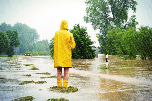 figure in rainstorm with back turned wearing a yellow raincoat and boots surrounded by flooding