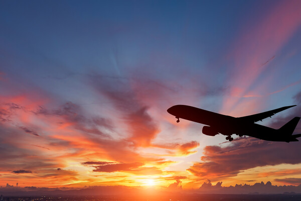 Silhouette of an airplane flying through a sunset 