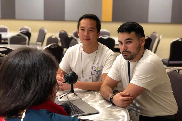 With a microphone between them, Enrique Lin-Shiao and Kevin Alicea-Torres sit for an interview with one of the subjects of their podcast. 