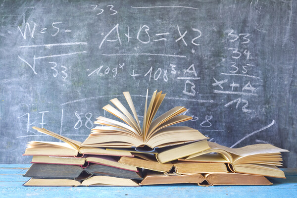 a stack of books in front of a chalkboard with math equations
