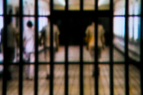 prisoners walking down hallway with prison bars in foreground