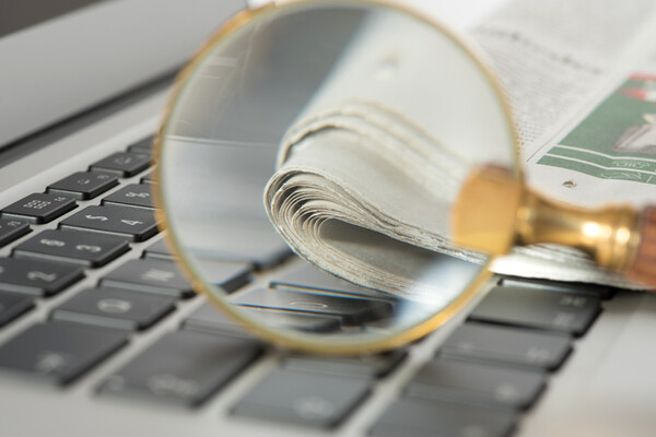 magnifying glass on top of laptop keyboard with newspaper visible through the glass