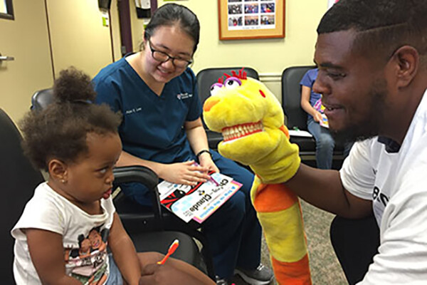 child at dentist office being mildly entertained yet skeptical of staff member with a yellow hand puppet