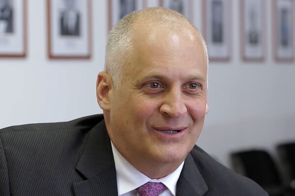 Smiling man in a grey suit with a purple tie.