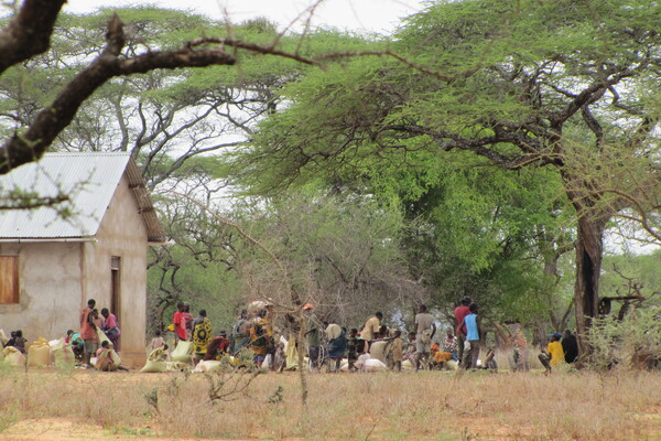A group of people, some holding sacks, next to a small rustic house and under trees