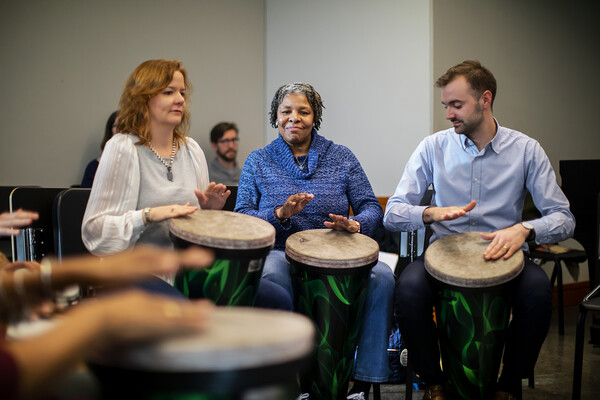 Two women and a man playing large bongo drums. 