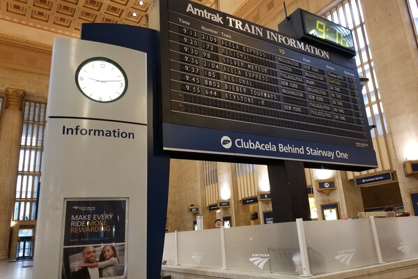 Split-flap board inside 30th Street Station surrounded by passengers and a clock