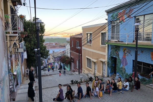 A group of college students sitting on a street between colorful buildings.