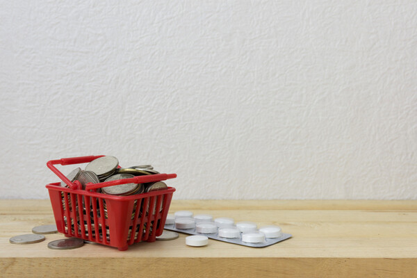 small shopping basket with coins and sleeve of pills on a shelf