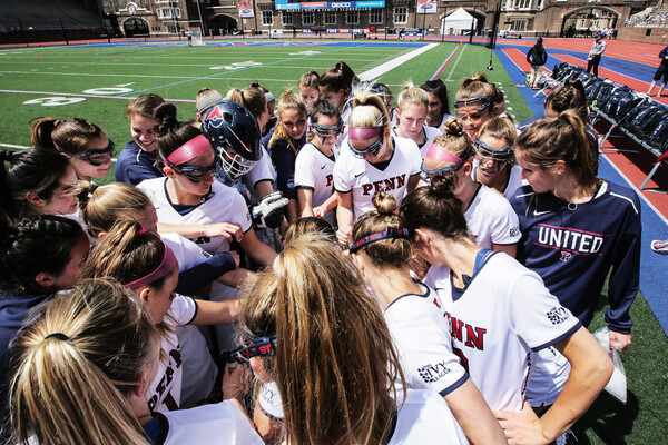 Women's lacrosse players put their hands in a circle on the sideline