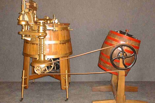 An old-fashioned washing machine, which looks like two wooden barrels on legs, next to each other and connected by large wiring.