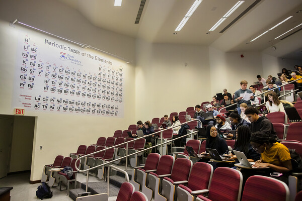 students in a classroom with a large periodic table behind their seats