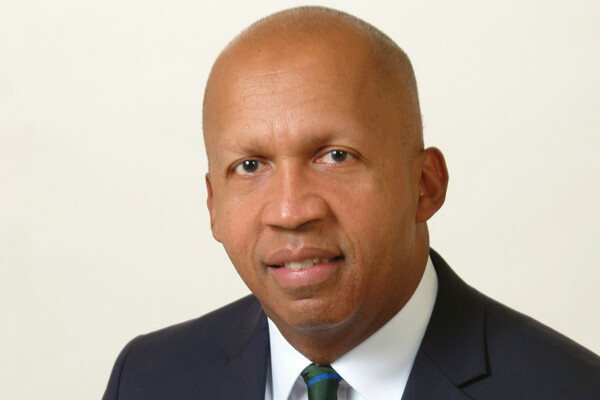 Bryan Stevenson wearing a black suit and green and blue striped tie.