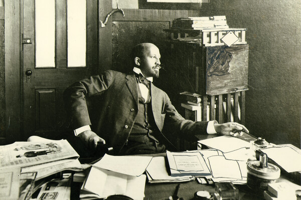 W.E.B. Du Bois sits at his desk in his office.
