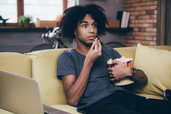 teenager watcing tv with popcorn on a couch looking surprised