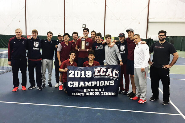 Men's tennis players and coaches pose with the 2019 ECAC Championship banner.