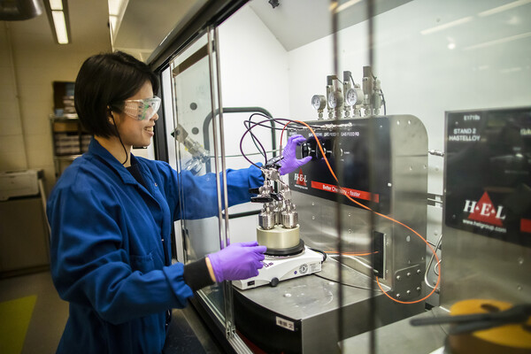 amy chu smiles while adjusting a knob on a metal piece of lab equipment