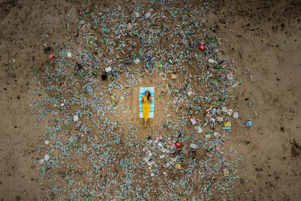 A person reclines on a chair on a beach surrounded by plastic bottles