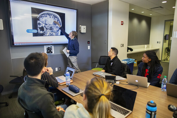 A man standing in front of a class of college students pointing to a scan of a brain.