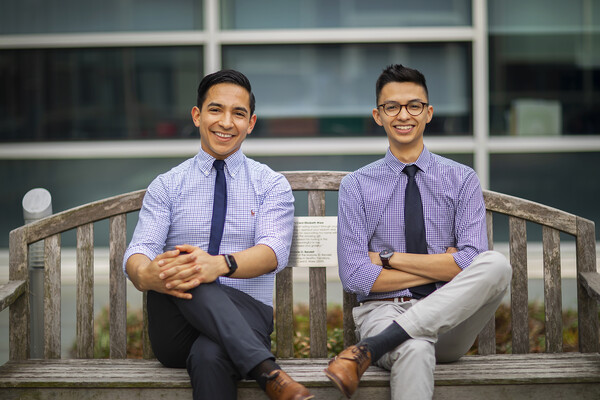 Two men sitting cross-legged on a wooden bench. 