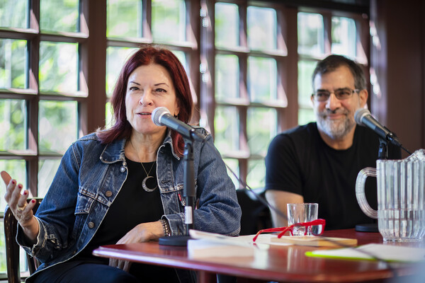 Rosanne Cash speaking at microphone at table with professor Al Filreis looking at her and smiling.