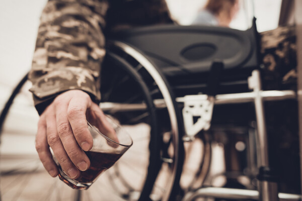 person wearing a camouflage jacket in a wheelchair holding a tumbler of alcohol