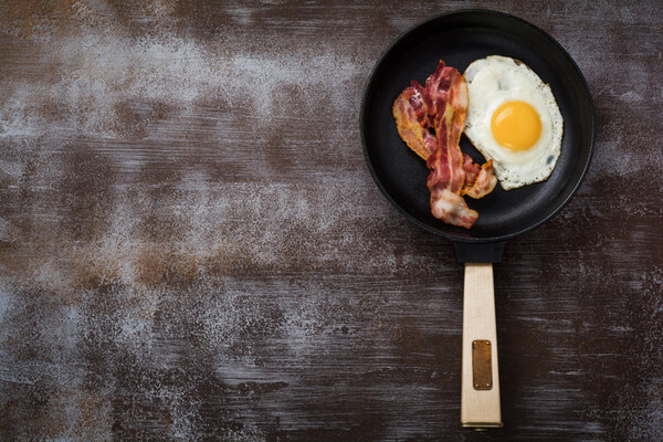 skillet on a table surface with one fried egg and two strips of bacon
