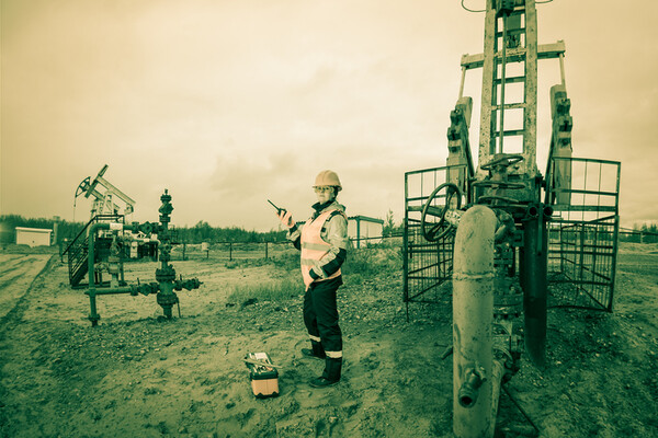 worker standing in oil field holding walkie talkie wearing a construction hat