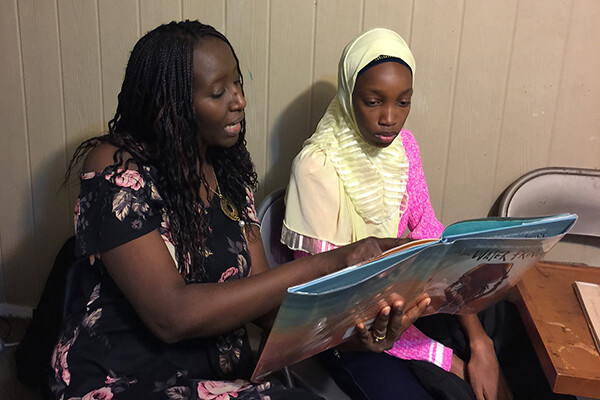 Aminata Sy sits with student reading a book to them.