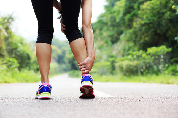 A stock photo of a woman holding her ankle while out for a jog on a road.