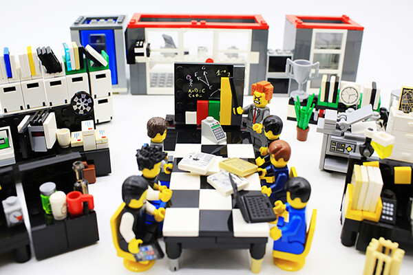 Lego figurines seated at a toy desk made to look like a business office