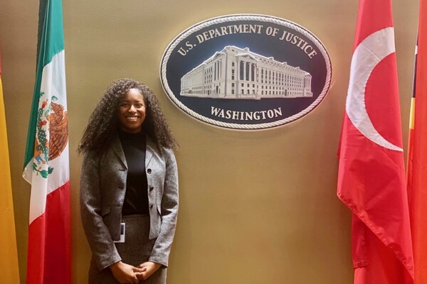 Student standing in front of plaque that says U.S. Department of Justice Washington, and flanked by two flags.