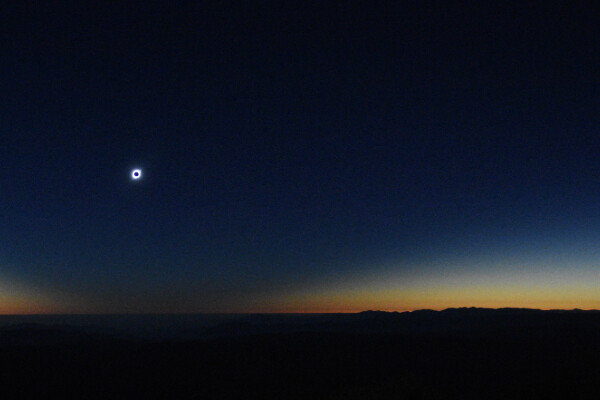 the sun covered by the moon during an eclipse, set against a darkening dusky sky with a black flat horizon in the foreground