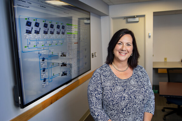 A smiling woman stands next to a screen that displays energy usage information for chiller plant system.