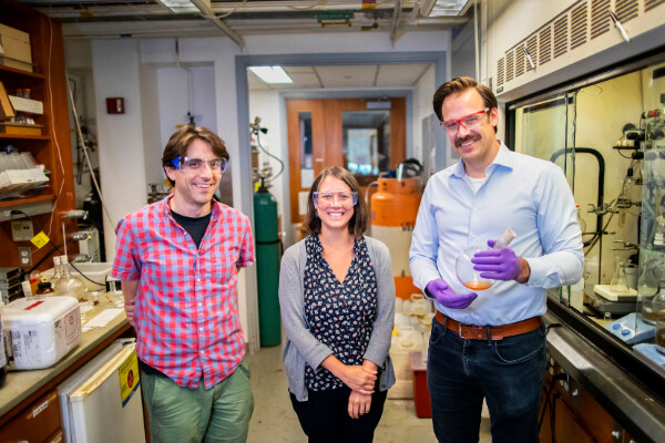 subotnik, anna, and schelter posing in a chemistry lab wearing googles, schelter is holding a round-bottomed flask