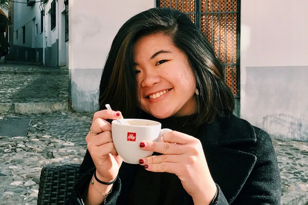 Student sitting outside holding a coffee cup and smiling.