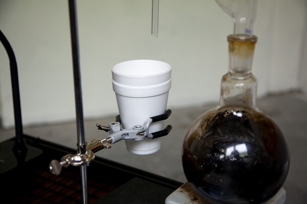 A styrofoam cup with liquid being dripped in from a distilling device