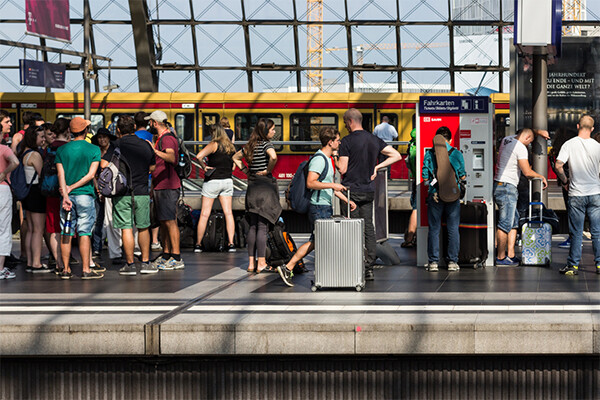 A group of people waiting on a platform of a train station with sunlit windows and a train on the tracks.