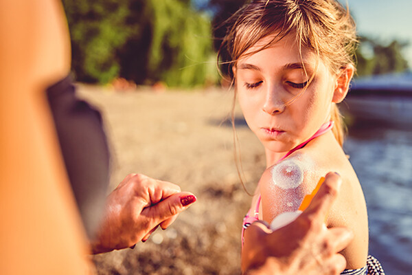 child looking at shoulder while parent sprays sunscreen on.