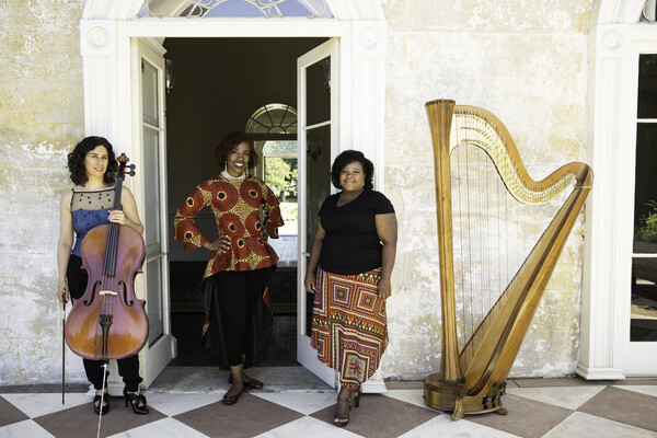 Three people posing by a doorway with a cello and harp