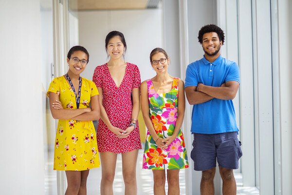 Four people in brightly colored clothing standing in a white hallway. 