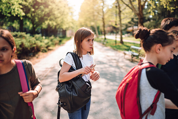 A young child with a backpack walks outside with three other students on their first day back at school.
